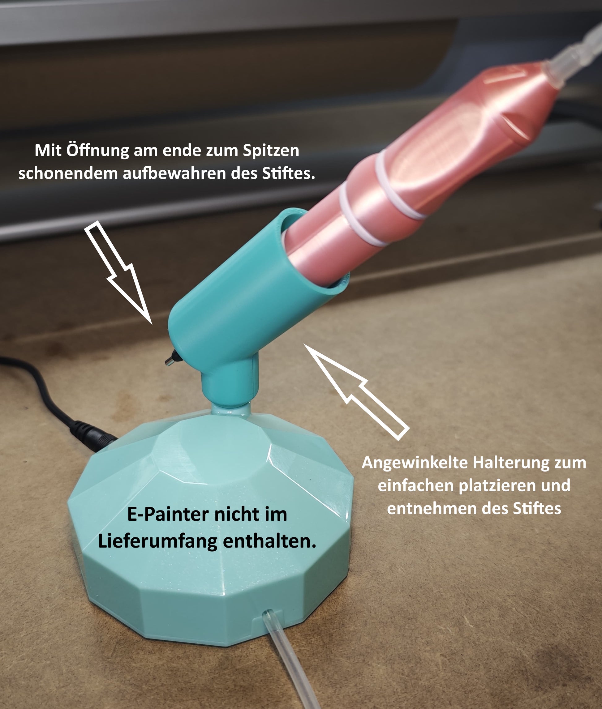 Ein blaugrünes und rosafarbenes stiftförmiges Werkzeug liegt in einem New Plastics Stifthalter für Ideen mit Herz E-Painter auf einer braunen Oberfläche. Der deutsche Text weist auf die Kompatibilität mit dem E-Painter hin, stellt aber klar, dass der E-Painter nicht im Lieferumfang enthalten ist.
