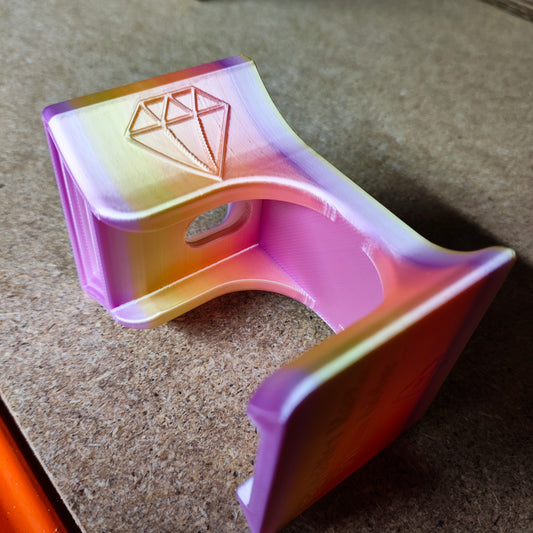 Ein 3D-gedrucktes Objekt von New Plastics, der Diamond Painting Trichter für runde Dosen, weist einen rosa, gelben und orangen Farbverlauf mit einem rautenförmigen Design auf. Auf Holz platziert, zeigt es geschwungene und eckige Elemente mit einem hohlen Zentrum zum präzisen Befüllen runder Behälter.