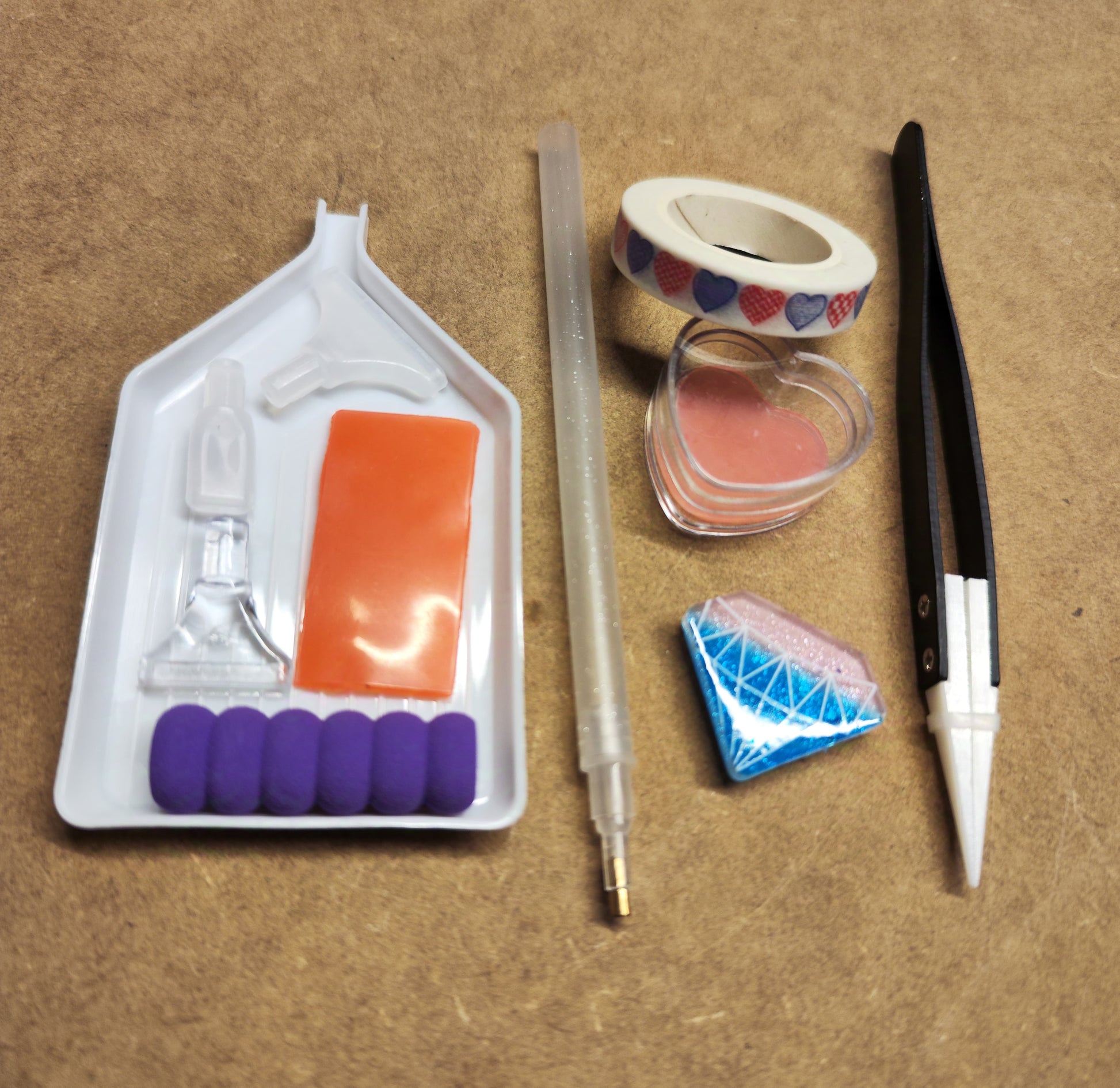 Das New Plastics Diamond Painting Tool-Kit enthält eine Schale, einen Stift, Wachs, eine Pinzette (Keramik-Pinzette), einen herzförmigen Behälter und Klebeband mit Herzmuster, alles elegant auf braunem Stoff angeordnet.
