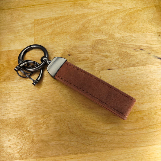 Ein neuer, personalisierter Schlüsselanhänger aus Leder aus Kunststoff, ein individueller Schlüsselanhänger aus braunem Leder mit Metallakzenten und einem kleinen Verschluss für Schlüssel, ruht auf einer Holzoberfläche.