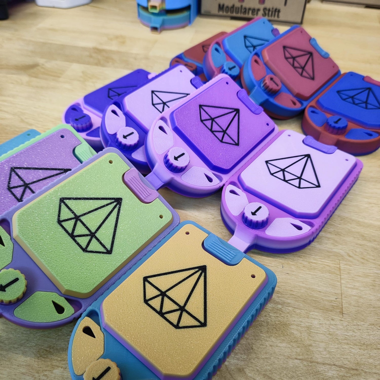 Modulare Gamecontroller in leuchtenden Lila-, Grün-, Blau-, Rot- und Orangetönen auf einem Holztisch weisen geometrische Designs auf, die an das Diamond Painting Schiffchen S1 von New Plastics erinnern.