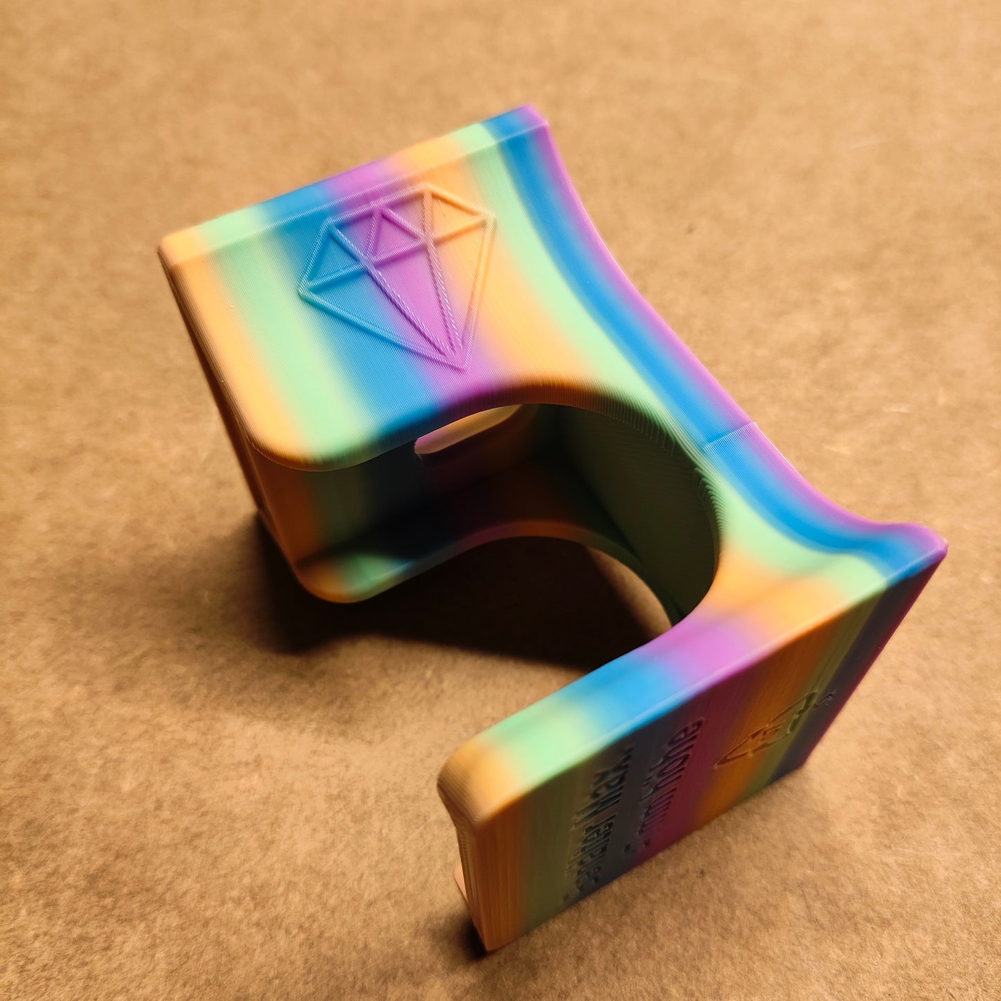 Der New Plastics Diamond Painting Trichter für runde Dosen ist ein 3D-gedrucktes Objekt mit einem Regenbogenverlauf auf Beige, hervorgehoben durch ein Diamantemblem. Er verfügt in der Mitte über eine U-förmige Öffnung zum präzisen, sauberen Befüllen oder Aufhängen.