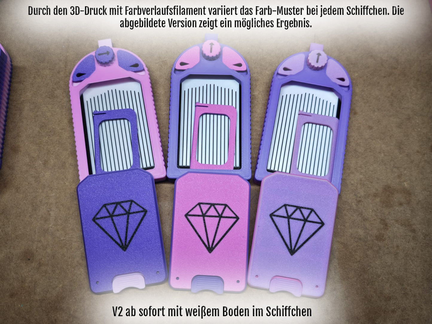 Drei lila- und rosafarbene Kartenhalter aus Kunststoff mit Edelsteinmotiven und teilweise herausgezogenen kammartigen Einsätzen erinnern an eckige Steinchen. Der deutsche Text beschreibt Farbvarianten für den 3D-Druck und die weiße Basis der V2-Version – ideal für die Organisation Ihrer Diamond Painting-Werkzeuge aus dem Diamond Painting Schiffchen S1 PLUS von New Plastics.