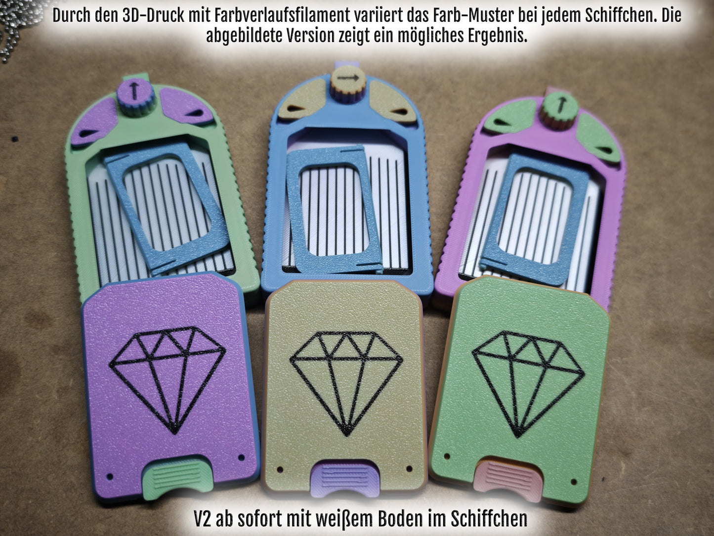 Drei 3D-gedruckte Schlüsselanhänger von New Plastics, genannt Diamond Painting Schiffchen S1, bestechen durch ihr leuchtendes Regenbogen-Gelb-Grün-Blau-Pink-V2-Design mit weißer Innenseite. Ein beschreibender deutscher Text hebt das multifunktionale Schiffchen hervor.