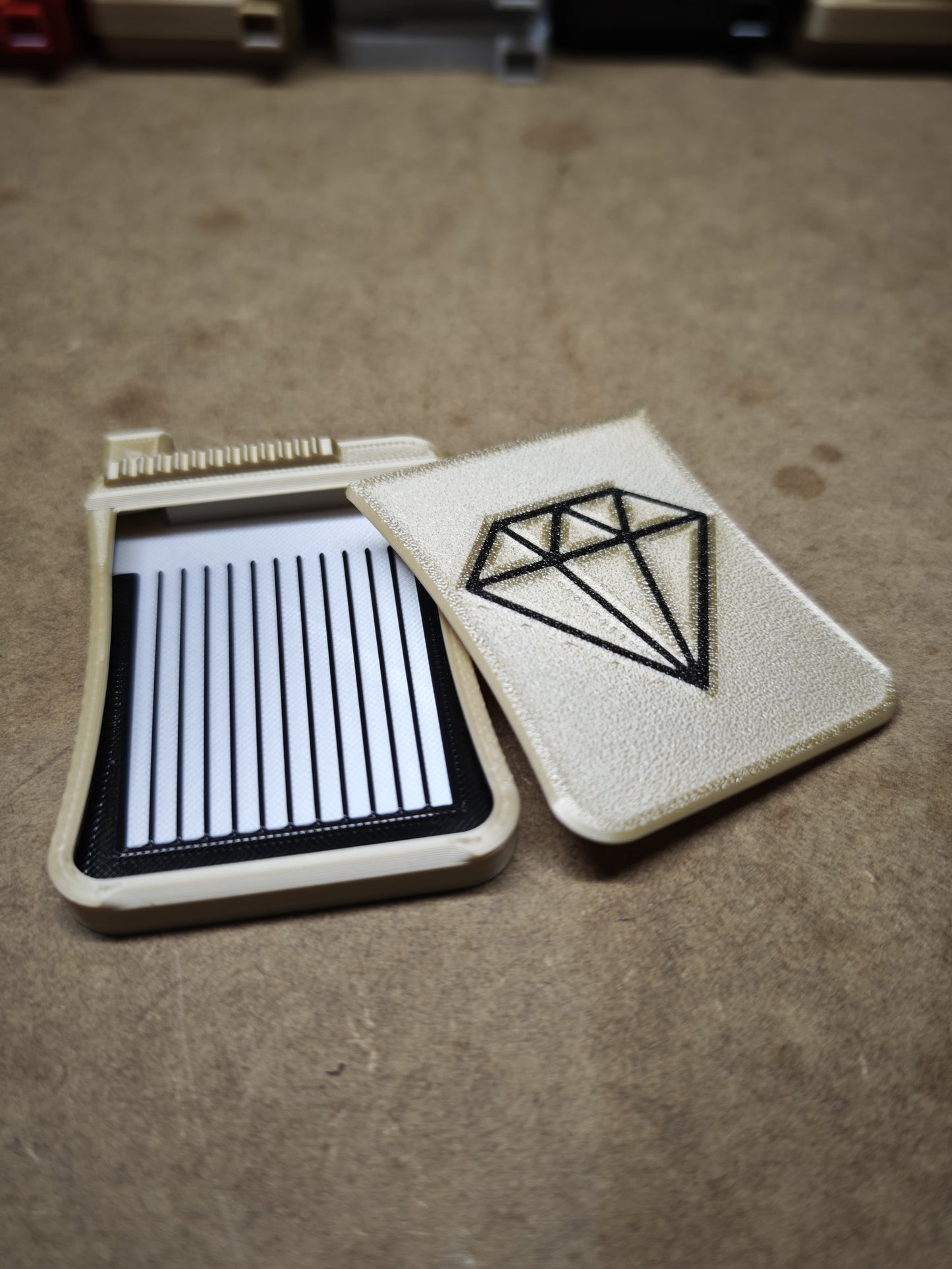 Ein rechteckiges, lederähnliches Etui mit Rautenmuster, ähnlich dem Diamond Painting Schiffchen S3 von New Plastics, verfügt über vertikale Schlitze in einem offenen Bereich, die alle auf einer braunen Oberfläche ruhen.