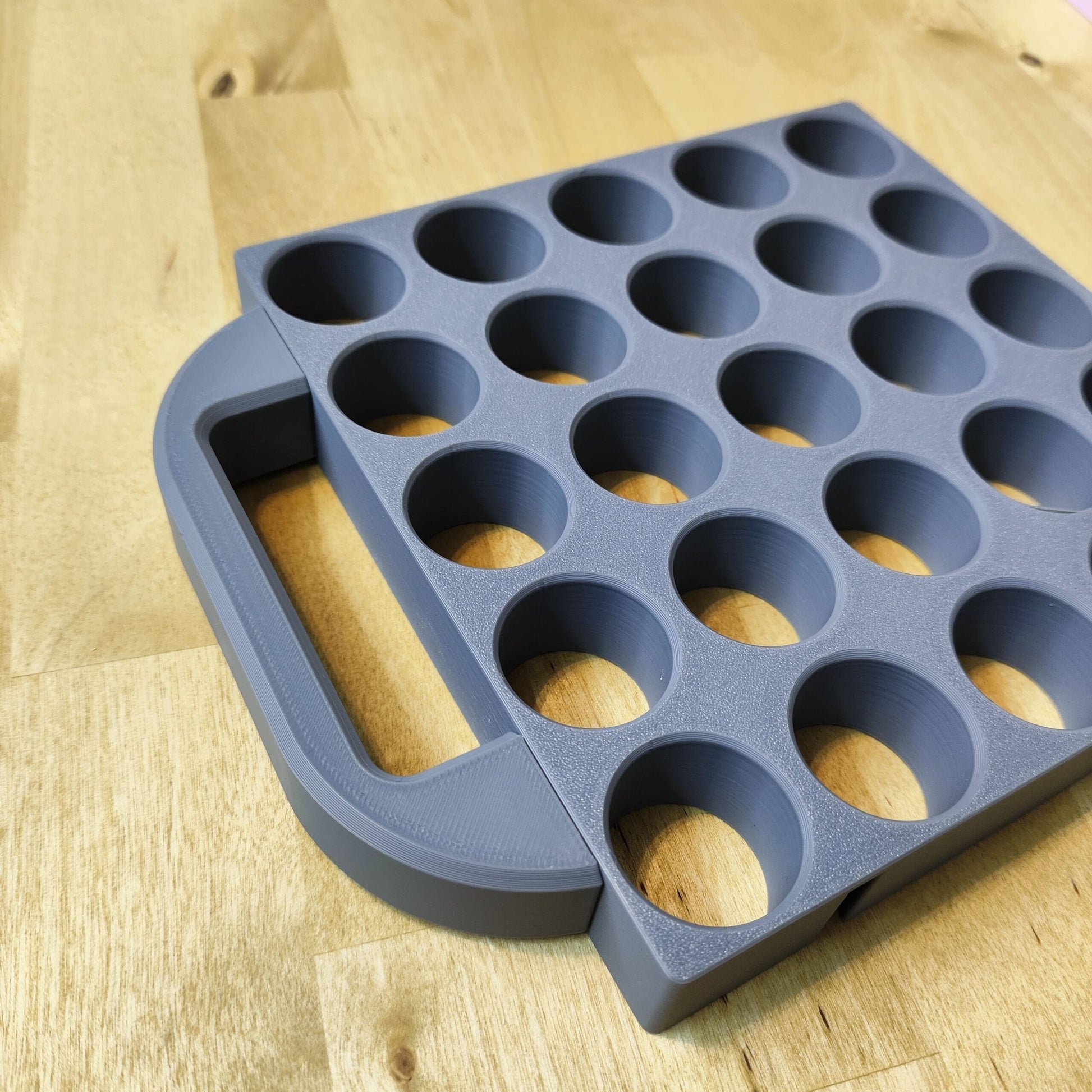 Ein graues, rundes Tablett von New Plastics mit mehreren gleichmäßigen runden Vertiefungen und einem Tragegriff für Steinchen Garage steht auf einer Holzoberfläche – ideal zum Backen, Basteln oder Aufbewahren von Zubehör für die Diamantmalerei.
