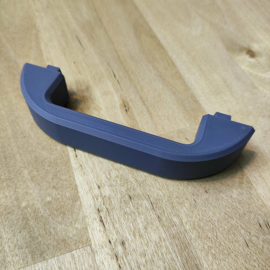 Ein blauer, U-förmiger „Tragegriff für Steinchen Garage“ von New Plastics ruht auf einer Holzoberfläche. Mit geraden, kurzen Seitenverlängerungen an jedem Ende bildet er einen schönen Kontrast zur sichtbaren Holzmaserung. Seine glatte Textur ergänzt sein praktisches Design.