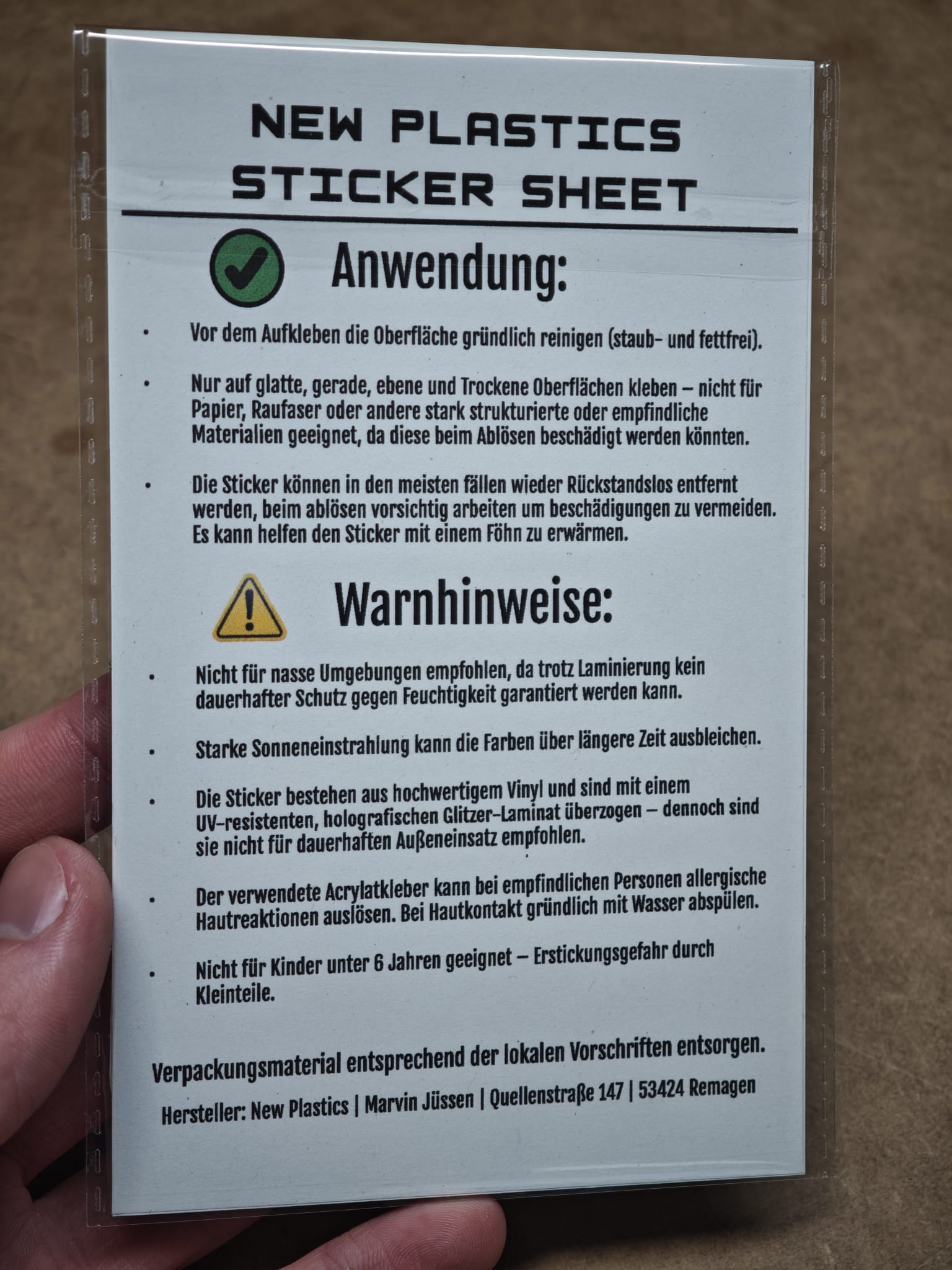Eine Hand hält eine deutsche Anleitungskarte für den New Plastics Diamond Painting Animals Stickerbogen mit 12 Stickern ca. DIN A6. Die Karte enthält Anwendungshinweise und Warnhinweise für DIY-Projekte mit grüner und gelber Hervorhebung.