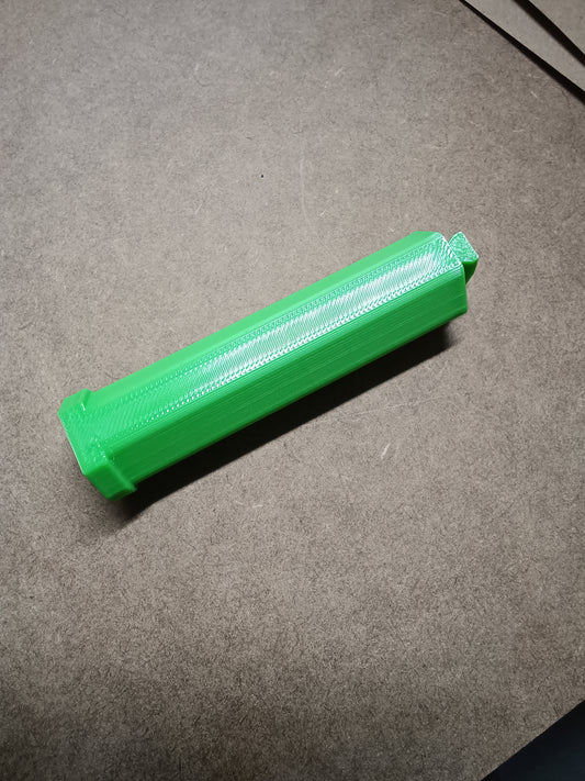 Ein grüner zylindrischer Gegenstand mit strukturierter Oberfläche, ähnlich der Washi Tape Halterung für Steinchen Garage von New Plastics, ruht auf einer braunen Holzoberfläche.