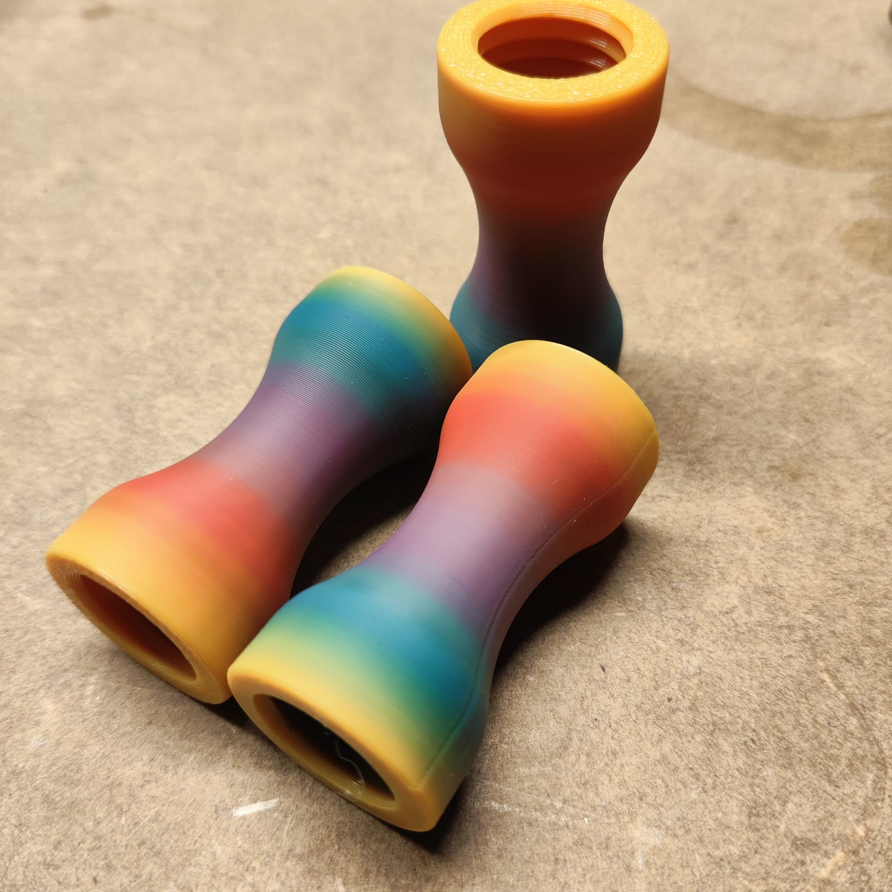 Drei Farbverlaufsspulen mit glatter Oberfläche, Teil des „Schmalen Griffstücks für Modularen Diamond Painting Stift“ von New Plastics, liegen auf einer strukturierten Oberfläche. Sie präsentieren Farben von Gelb bis Lila und eignen sich ideal zur Verschönerung Ihrer künstlerischen Projekte, solange der Vorrat reicht.