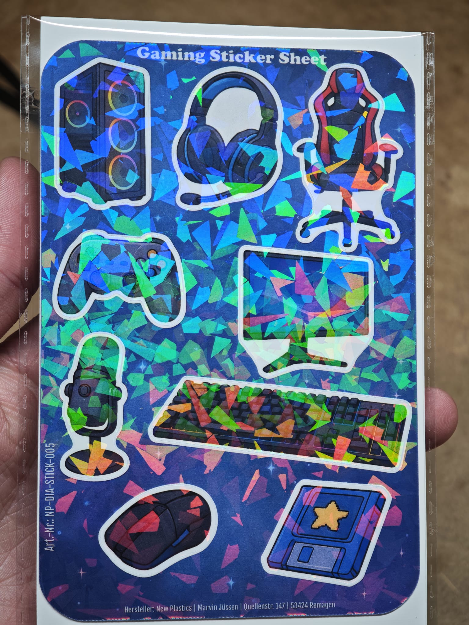 The New Plastics Gaming Sticker Sheet mit 9 Stickern ca. DIN A6 zeigt holografische Motive wie Lautsprecher, Kopfhörer, Gamingstuhl, Controller, Monitor, Maus, Tastatur, Mikrofon und blaue Gaming-Karte – ideal für DIY-Projekte!.